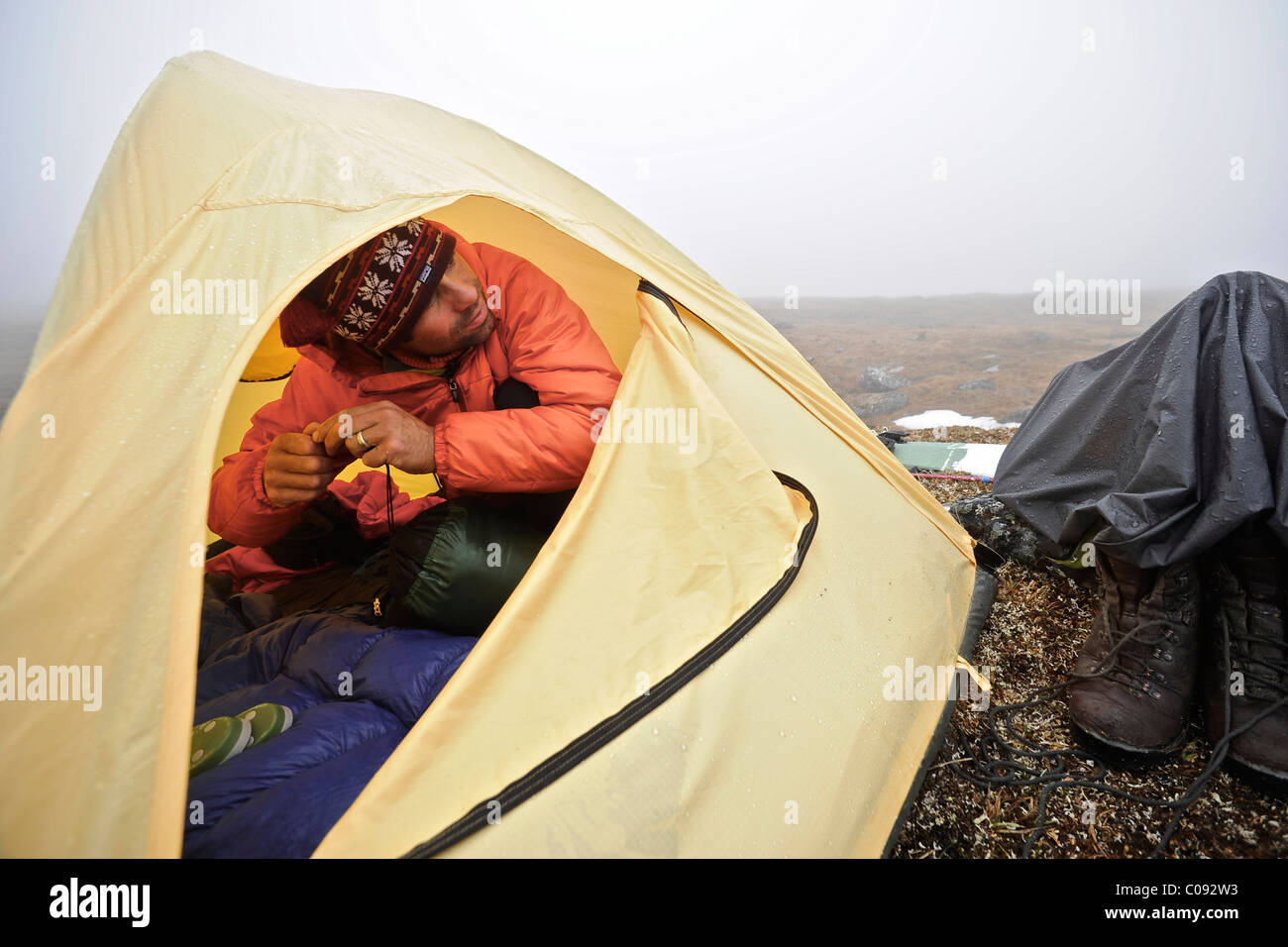 Backpacker sits inside a tent and waits out inclement weather at an alpine camp below Mt. Chamberln, Brooks Range, ANWR Stock Photo