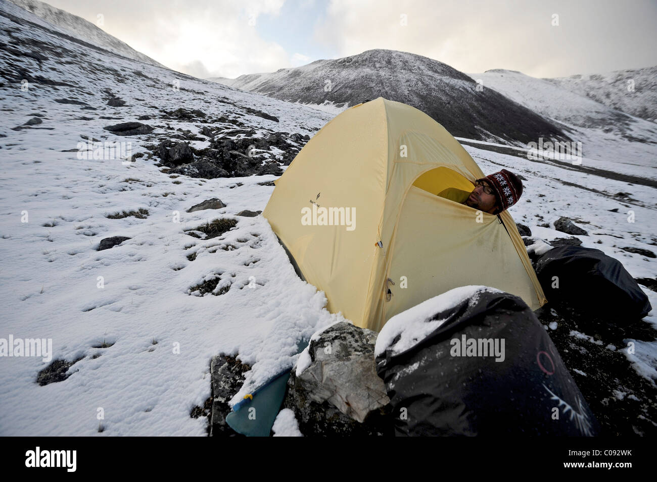 Backpacker sits inside a tent and waits out inclement weather at an alpine camp below Mt. Chamberln, Brooks Range, ANWR Stock Photo