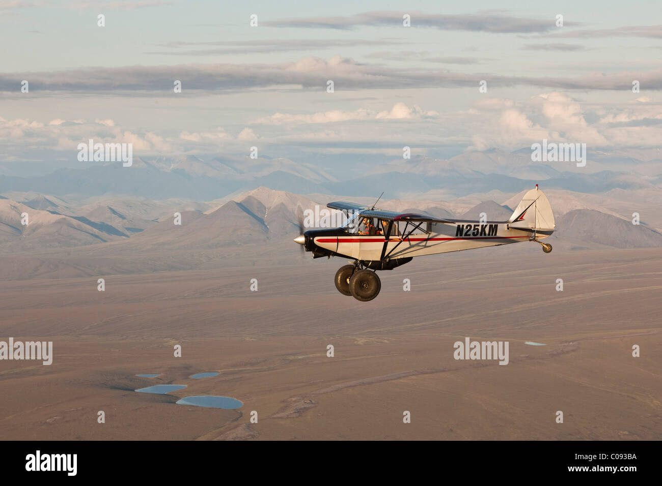 Aerial view of a Piper Super Cub airplane flying over the Jago River with the Romanzof Mountains in the background, ANWR Alaska Stock Photo