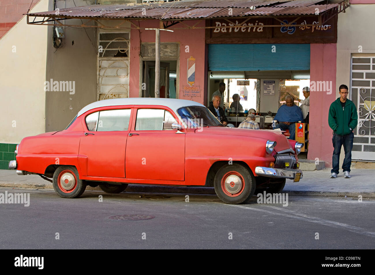 An old American 1950s red automobile parked outside a barbers in a street in Havana  Cuba Stock Photo