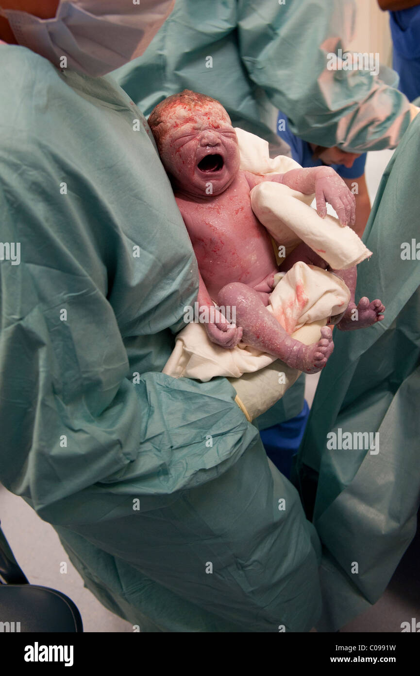 A just delivered screaming new born Caucasian baby takes its first breaths in the arms of a doctor in theater Stock Photo