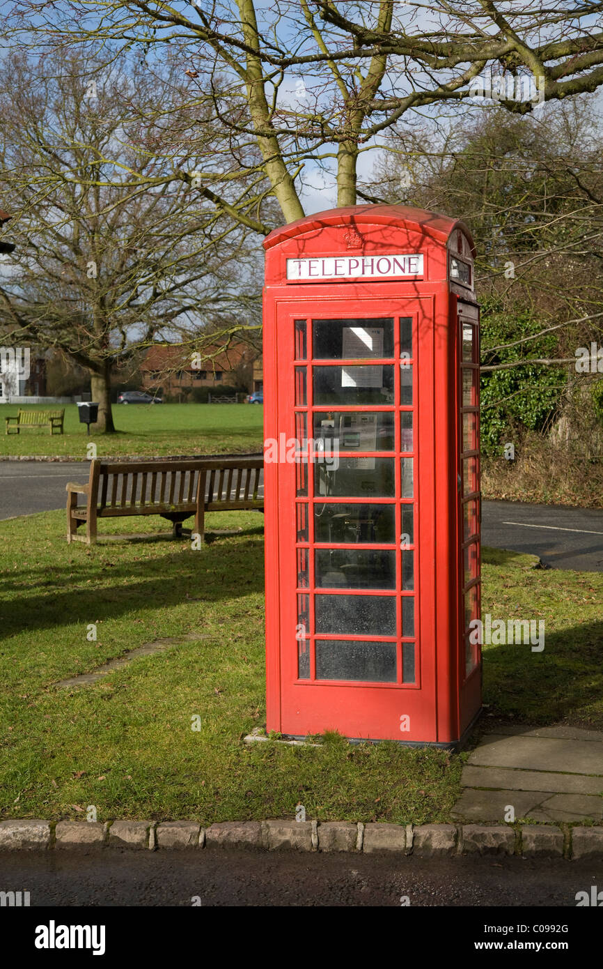 An original red telephone / coin operated phone call box on a grass verge, near a park bench, in Holyport, Berkshire. UK. Stock Photo