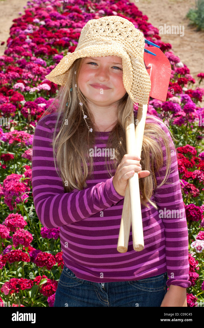 Girl, 8 years old, standing with spade and rake in a field of Sweet William carnations Stock Photo