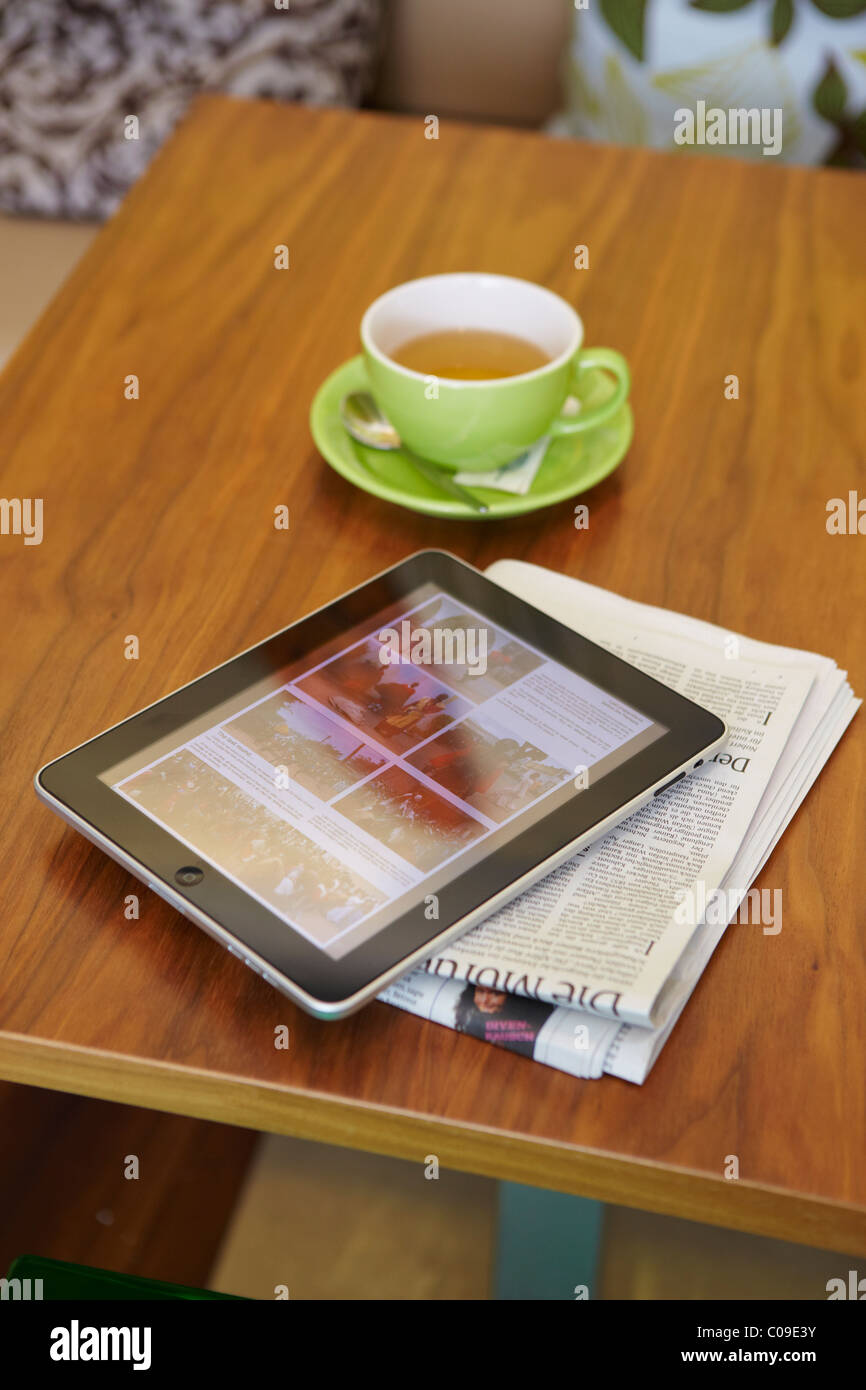 IPad tablet computer with a teacup and a newspaper on a wooden table Stock Photo