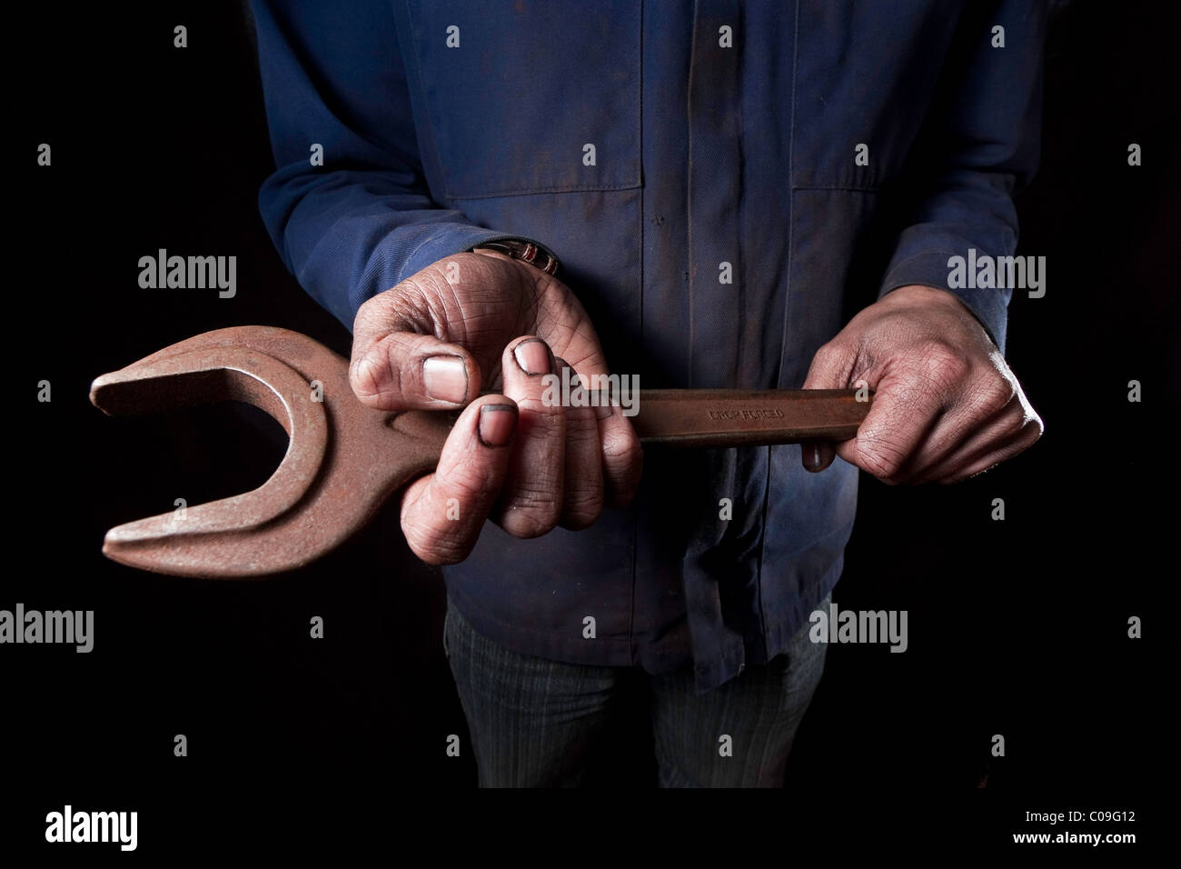 Dirty oil covered hands holding a large rusty spanner. Stock Photo