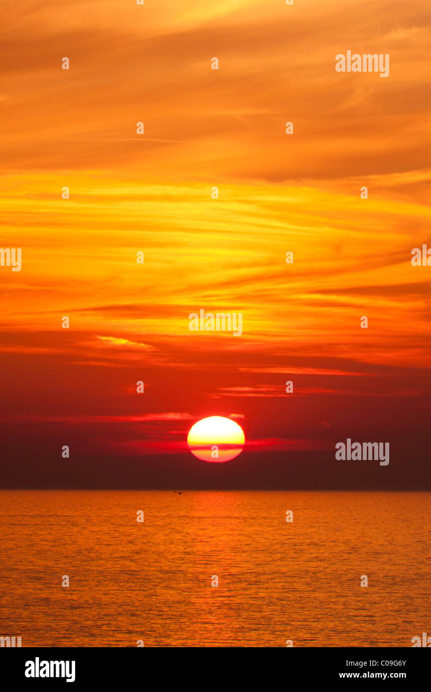 Full setting sun sunset in reed and orange over the sea with swirling clouds. Stock Photo