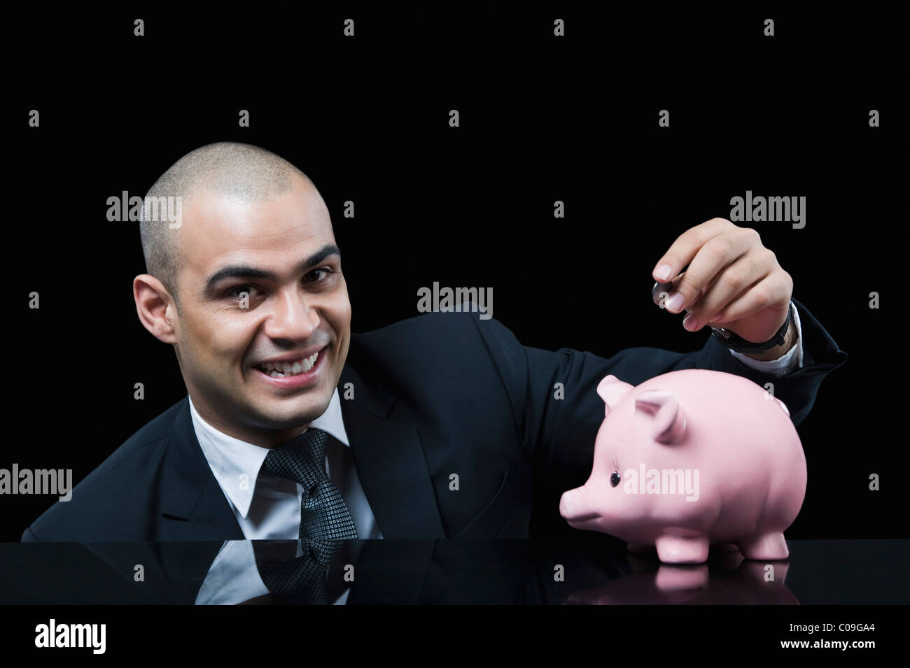 Businessman inserting a coin into a piggy bank Stock Photo - Alamy