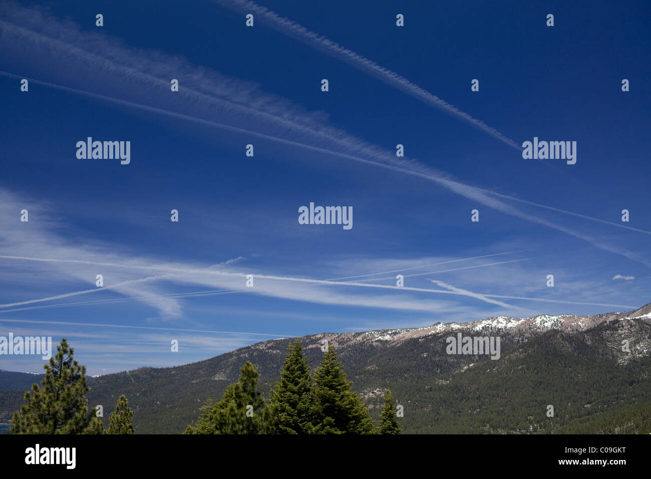 Vapor trails from high-flying jet airplanes in blue sky above Lake Tahoe on the border between California and Nevada Stock Photo