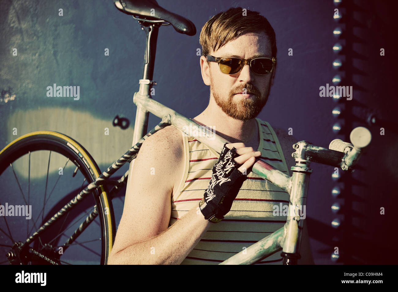 A fixed gear rider in a yellow striped tank top and sunglasses poses. Stock Photo