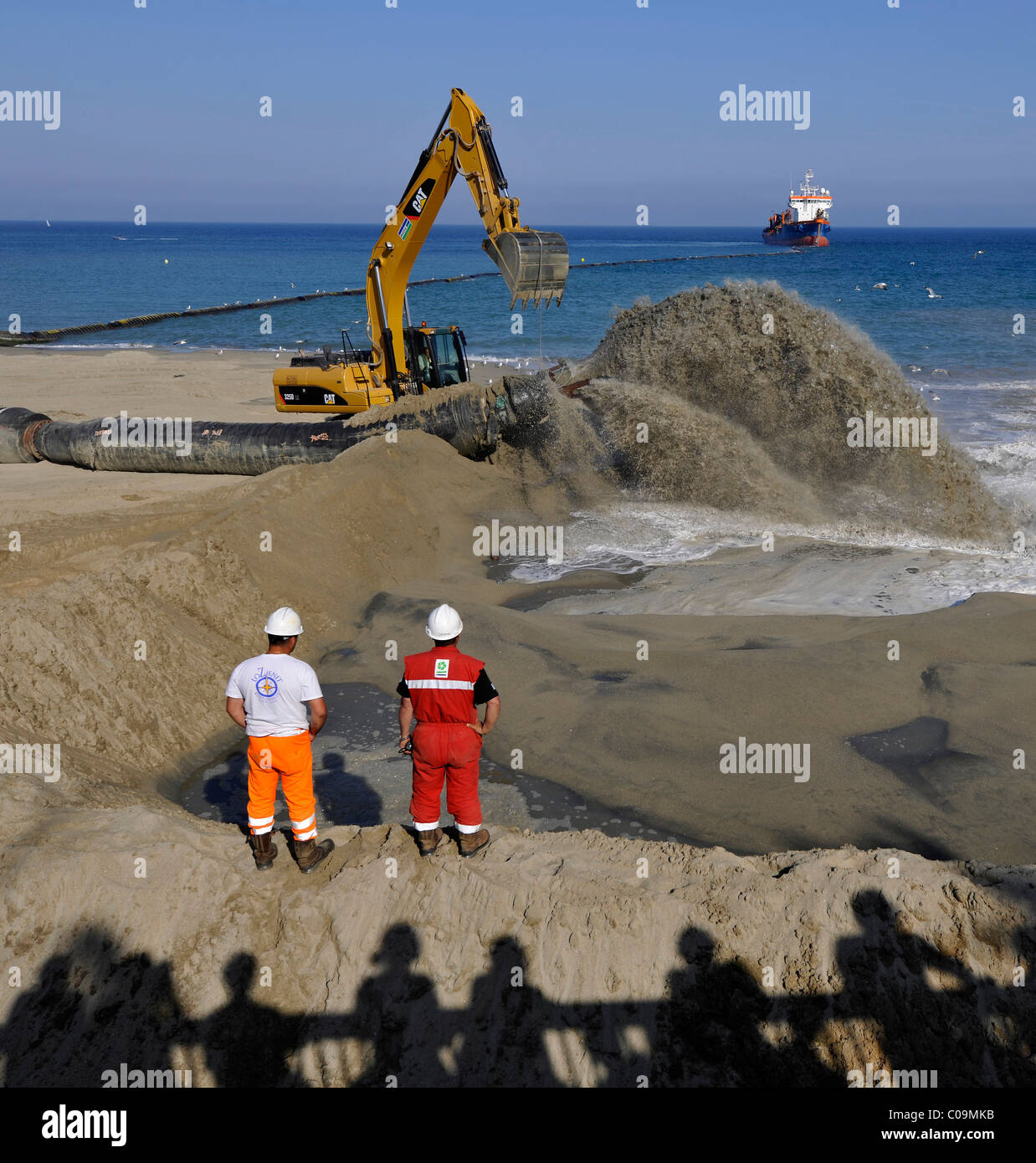 Onlookers watching while a dredger is pumping sand through a hose onto a beach for beach nourishment or beach replenishment Stock Photo