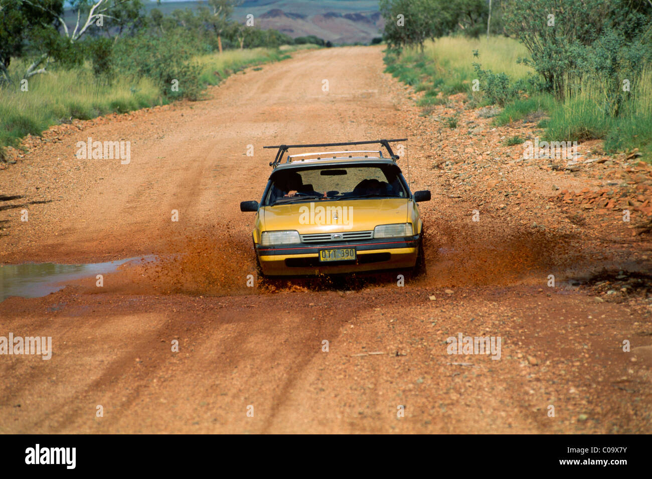 Car driving through a puddle on a red dirt road, Western Australia, Australia Stock Photo