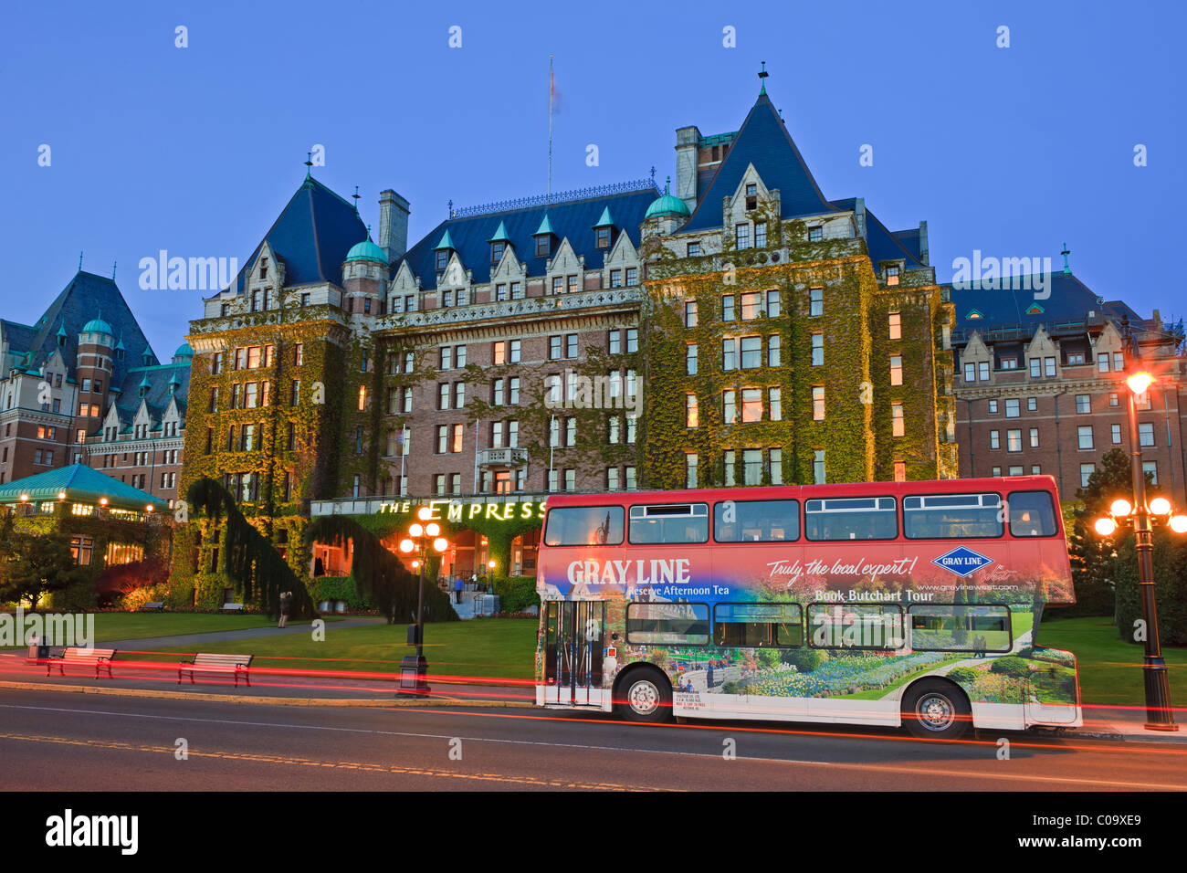 The Empress Hotel, a famous landmark in the Inner Harbour in Victoria, illuminated at twilight with a red tour bus Stock Photo
