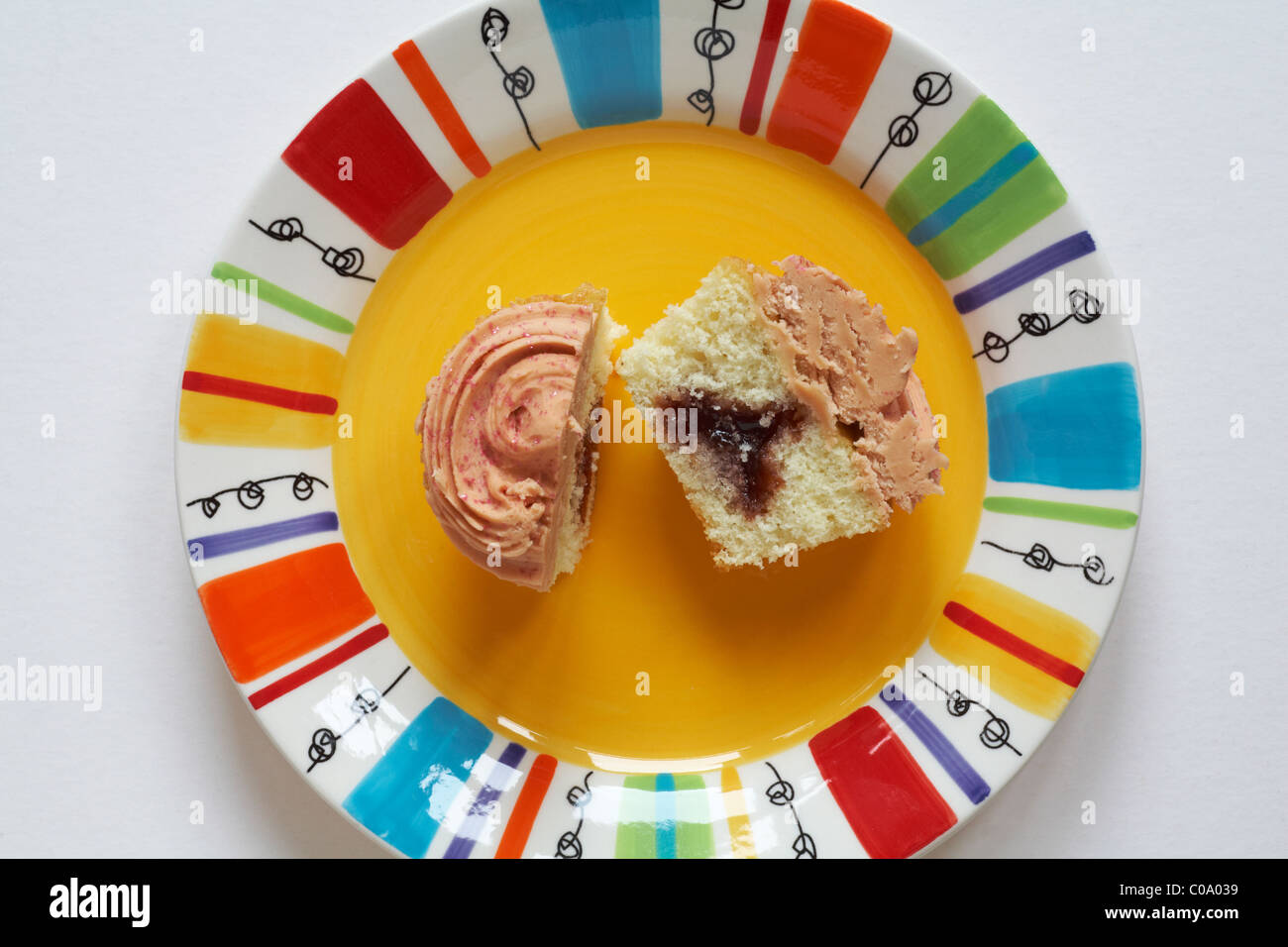 looking down on Marks & Spencer strawberry and vanilla cupcake cut in half on brightly coloured yellow plate - from above Stock Photo
