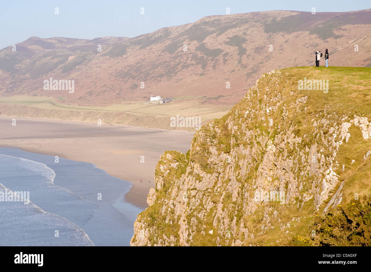 Two people are dwarfed by the cliffs at Rhossili on the Gower near Swansea, Wales. Stock Photo