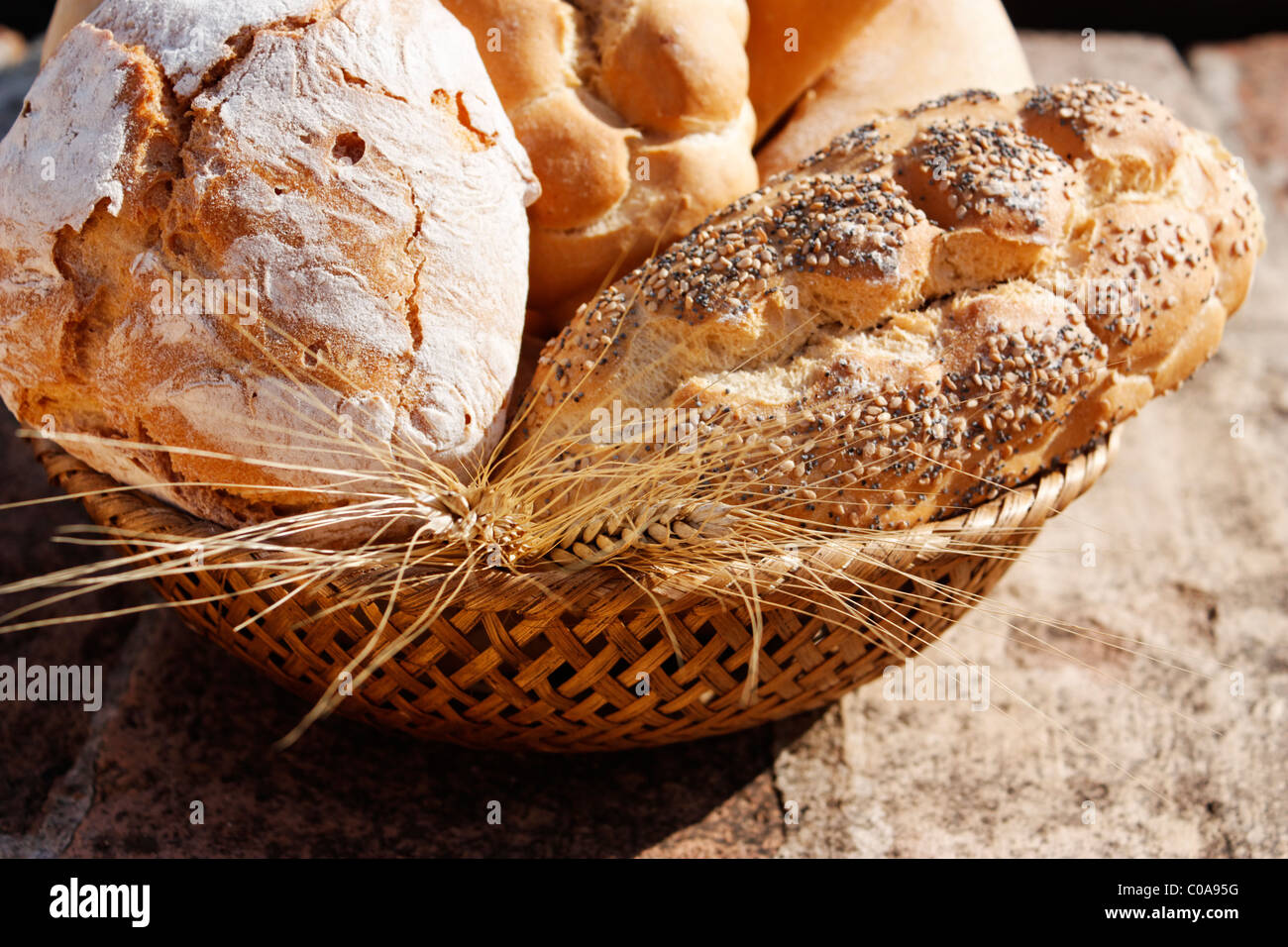 A close-up of a bread basket with a variety of breads and wheat on stone table. Stock Photo