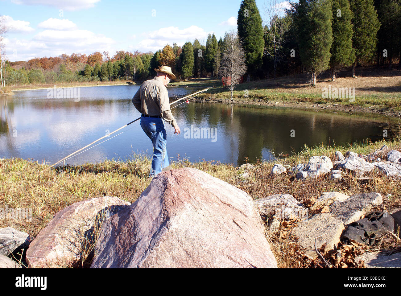 Man walks along lake looking for perfect fishing spot with cane pole. Stock Photo