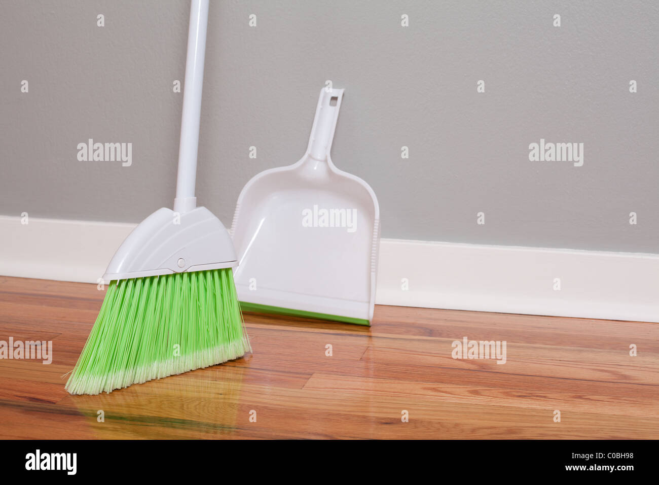 Green Broom And Dust Pan On Hardwood Floor Stock Photo