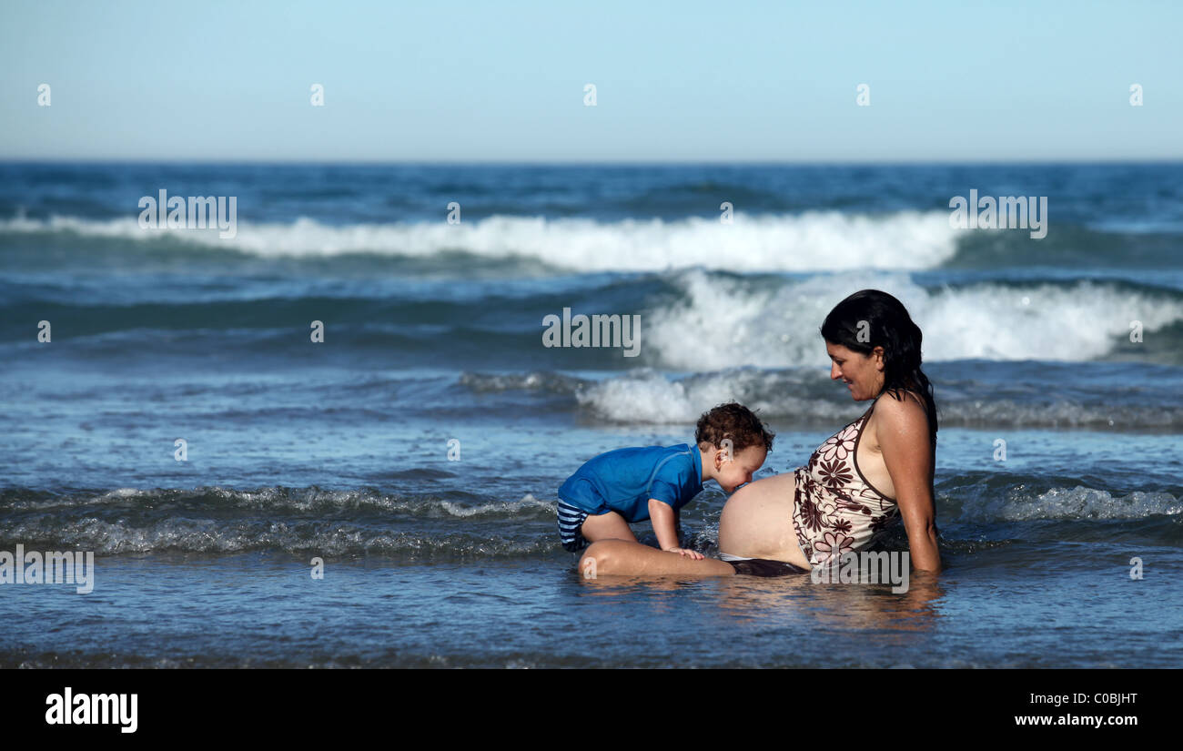 Toddler kissing his pregnant mothers belly. Stock Photo