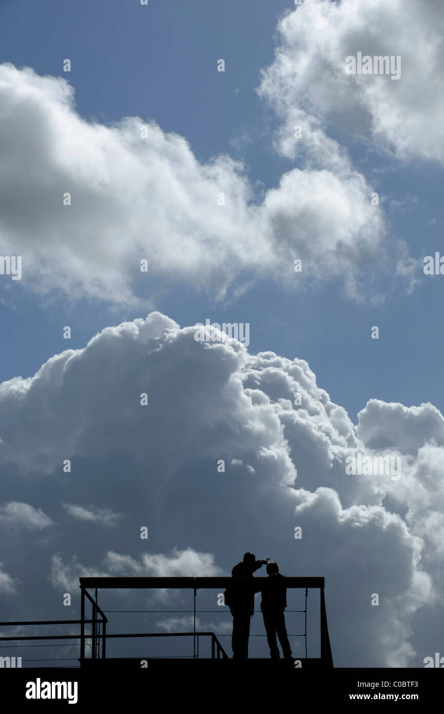 Silhouettes of a man pointing something out to a child before a cloudy sky Stock Photo