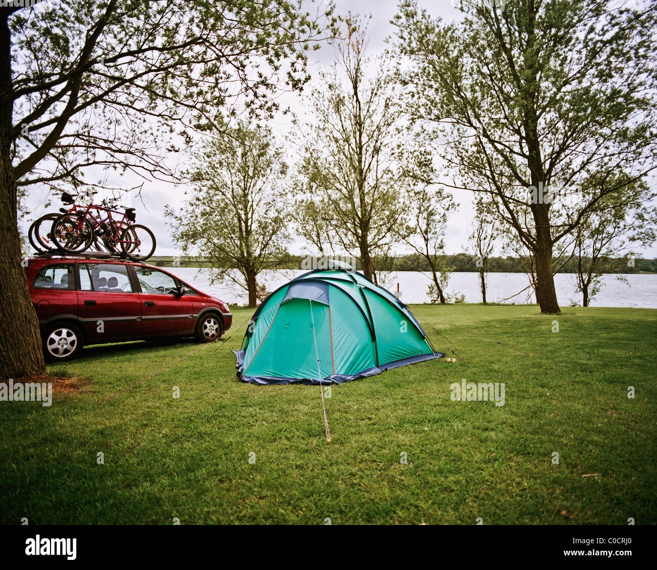 A tent erected next to a river with a car and bicycles Stock Photo