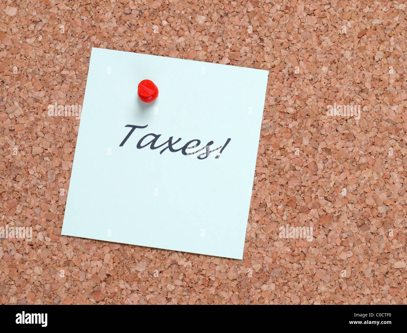 Paper memo note with TAXES word affixed to corkboard Stock Photo