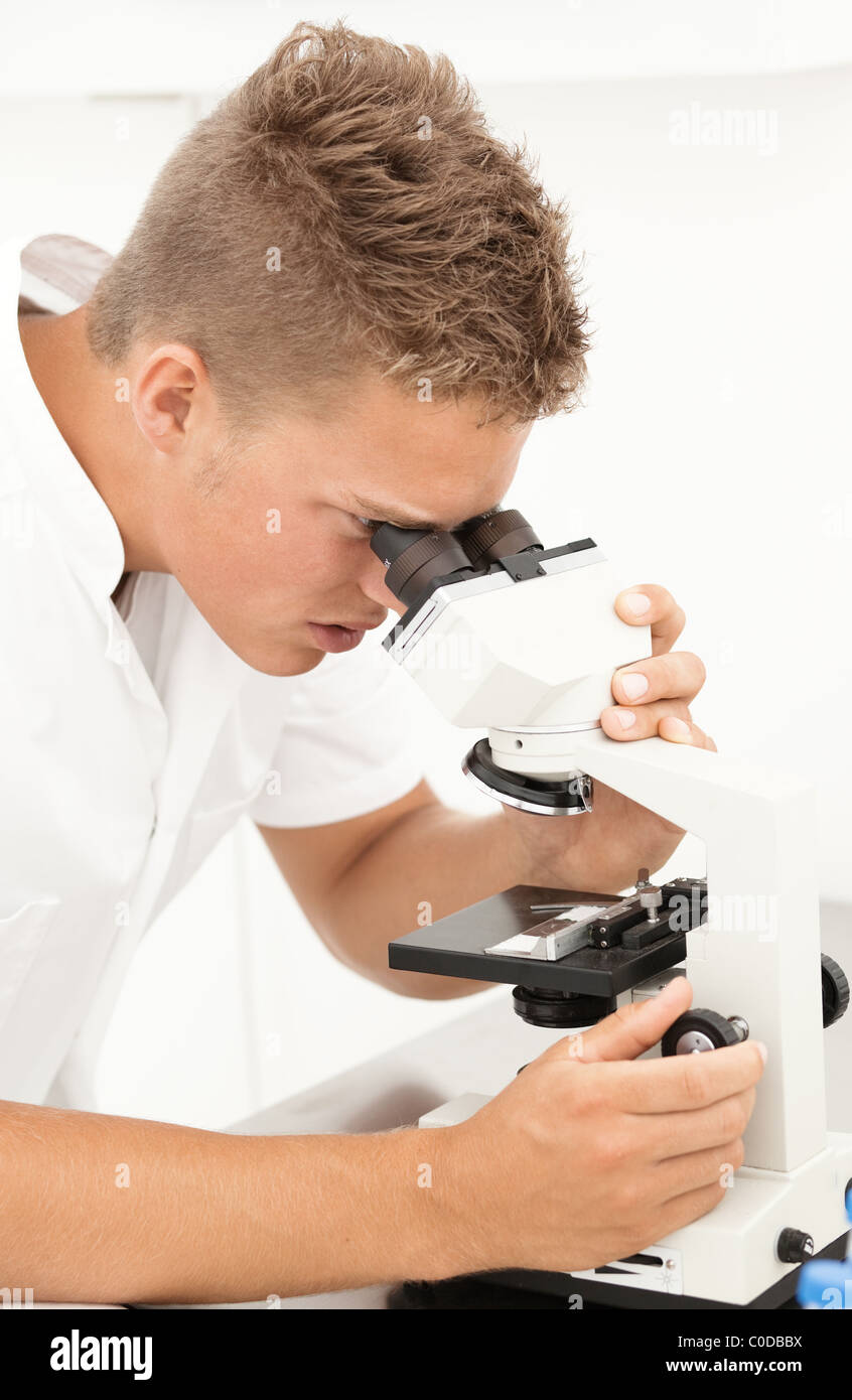 Young blond researcher concentrated on picture in his microscope Stock Photo