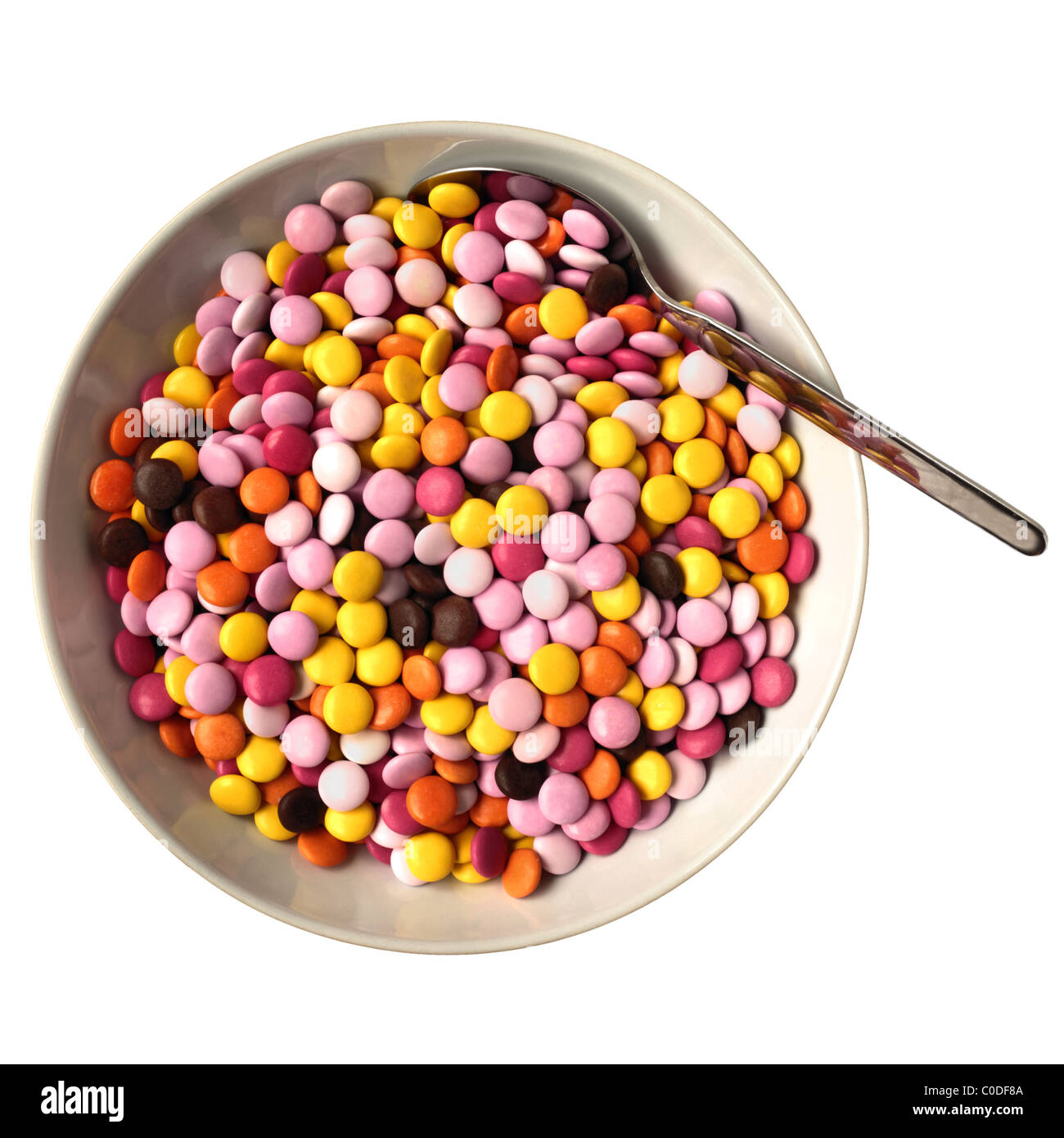 A round bowl of candy coated chocolates with a spoon on a white background Stock Photo