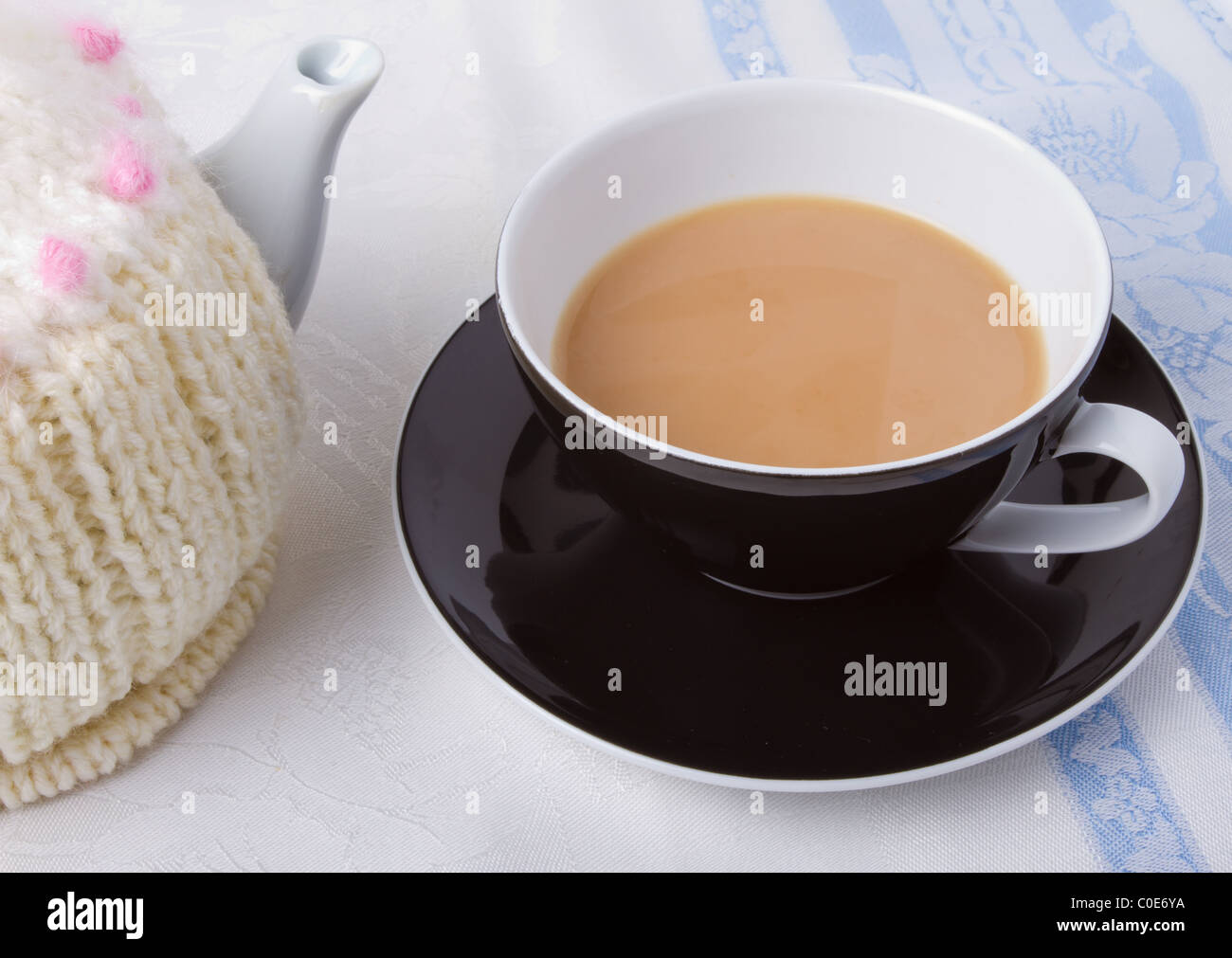 Cup of tea with tea pot and knitted tea cosy. Stock Photo