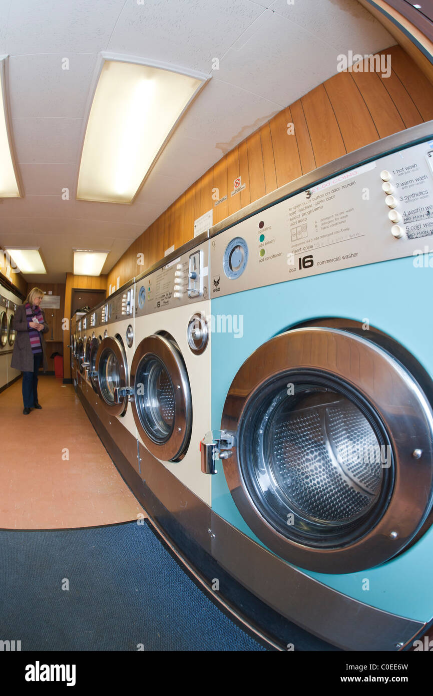 A laundrette with commercial washing machines and a MODEL RELEASED woman waiting for her washing in the background in the Uk Stock Photo