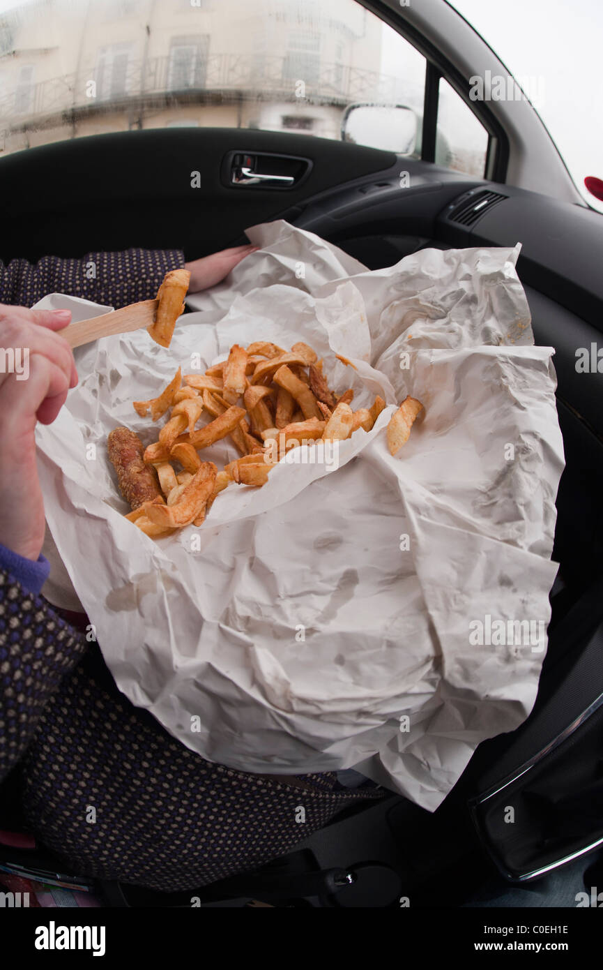 A woman eating fish and chips wrapped in paper inside a car in the Uk Stock Photo