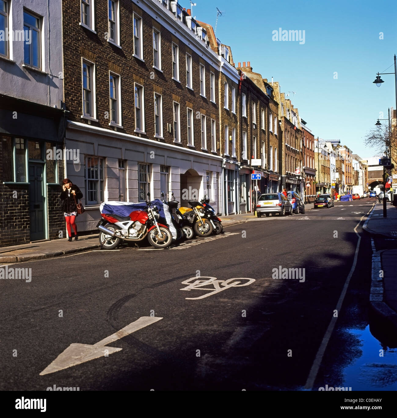 A woman on her mobile phone walking past motorcycles parked on Bermondsey Street, South London SE1 England UK Stock Photo