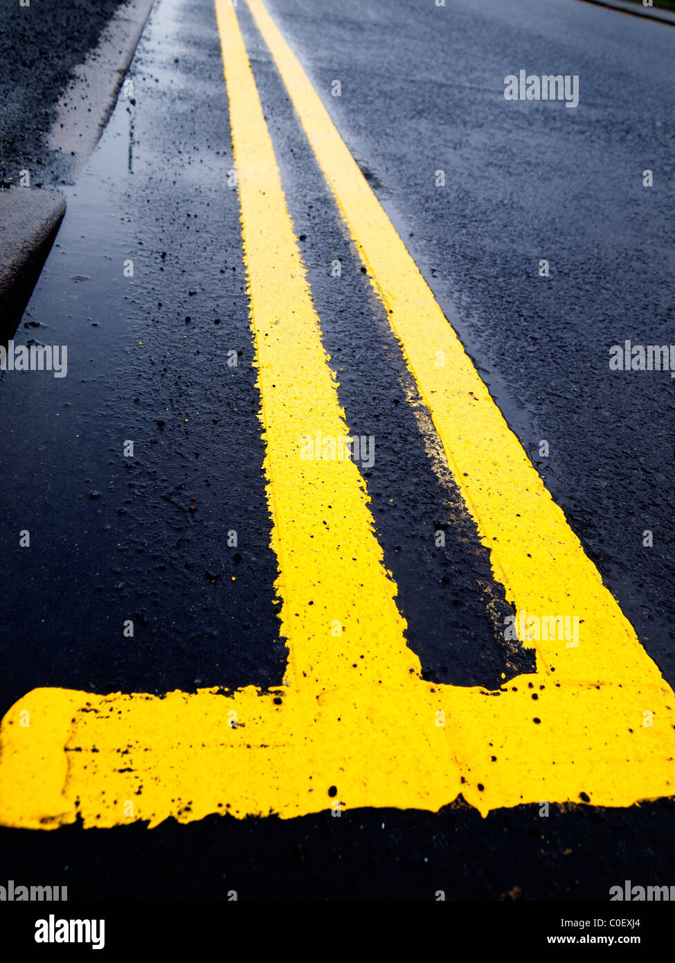 Road marking a newly painted double yellow line on a wet road Stock