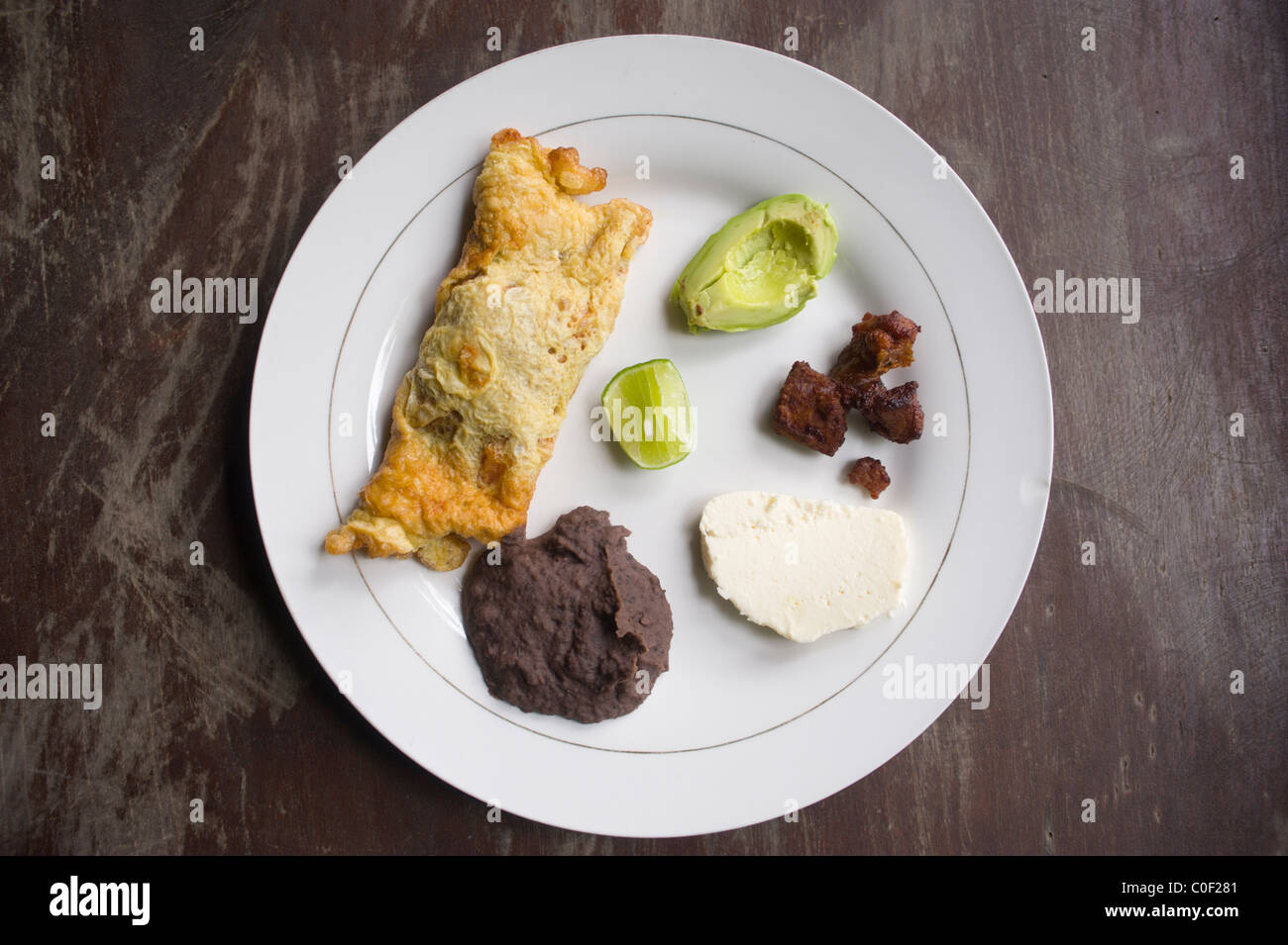 Selection of foods from Honduras. Omelette filled with vegetables, Refried beans, Fresh Cheese, Chicharrón, Avocado and lime. Stock Photo