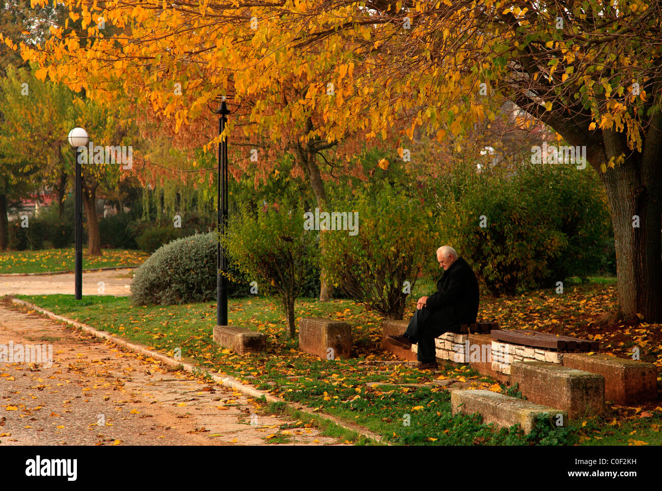 A lonely old man sitting skeptical and melancholic on a bench on the lakeside road of Ioannina, Epirus, Greece Stock Photo