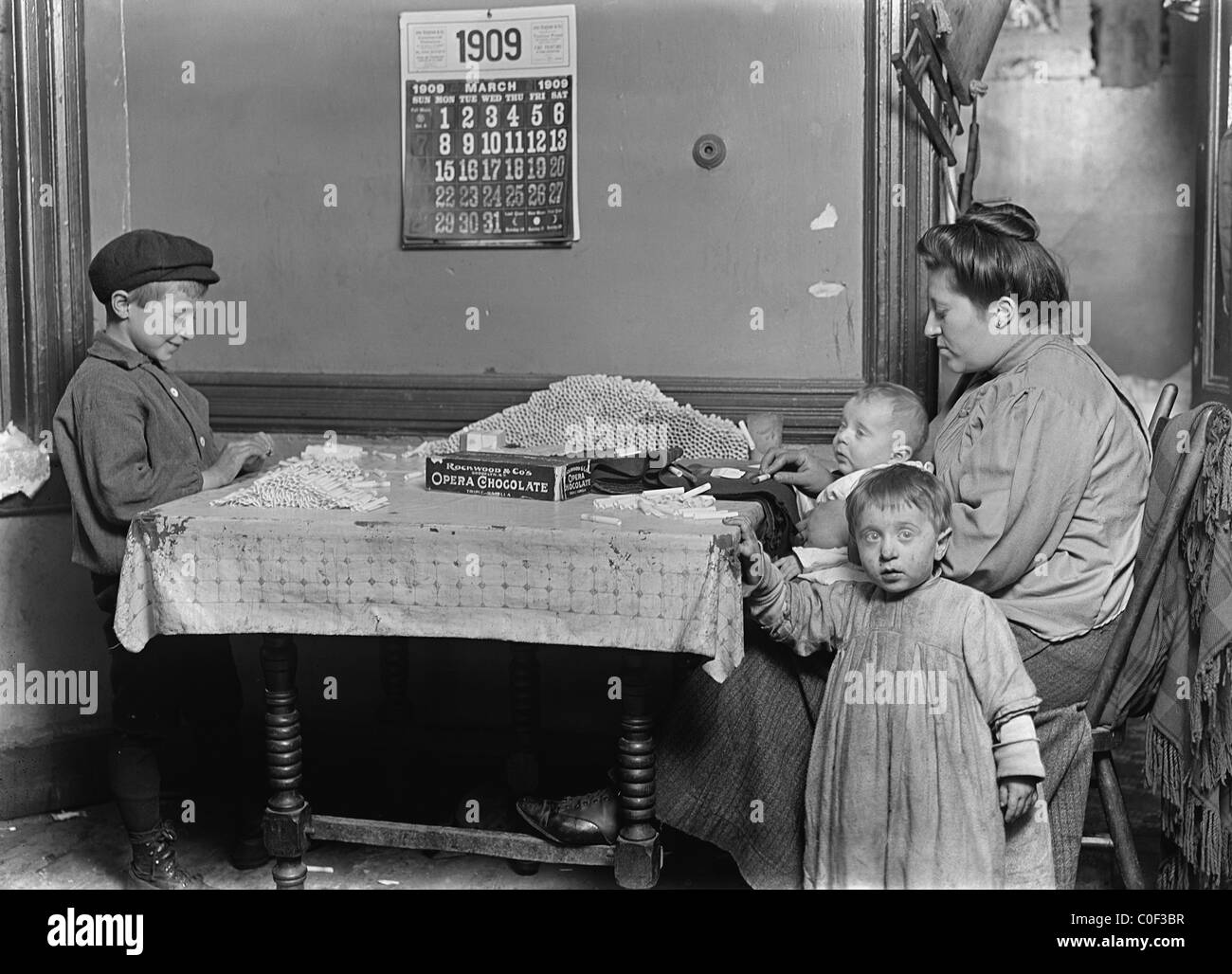 Widow & boy rolling papers for cigarettes in a dirty tenement. Location New York City 1908 Stock Photo