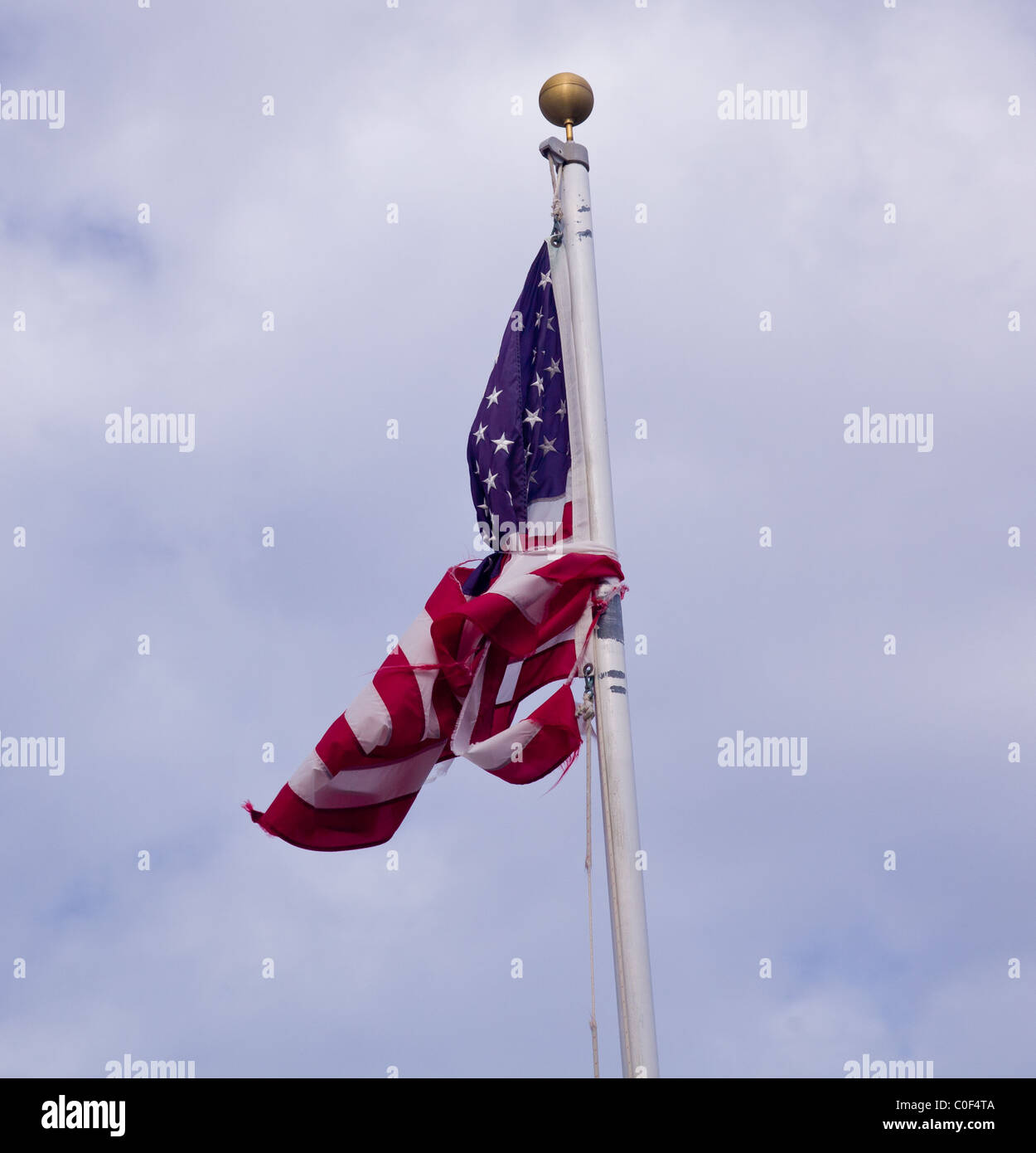 Unusual picture of US stars and stripes flag tied into a knot against the flag pole and torn Stock Photo