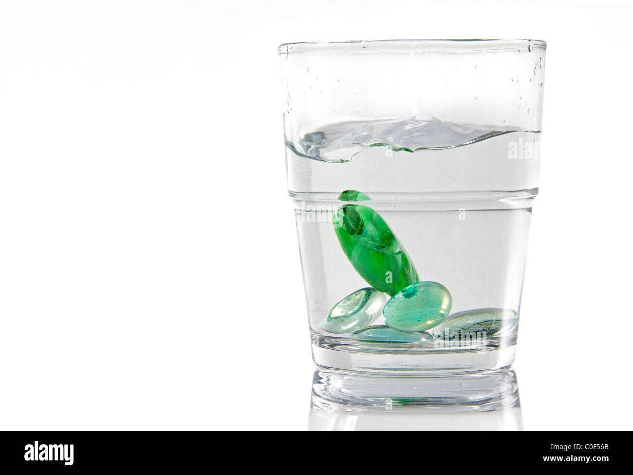 Marbles being dropped in a glass of water. White background isolated image Stock Photo
