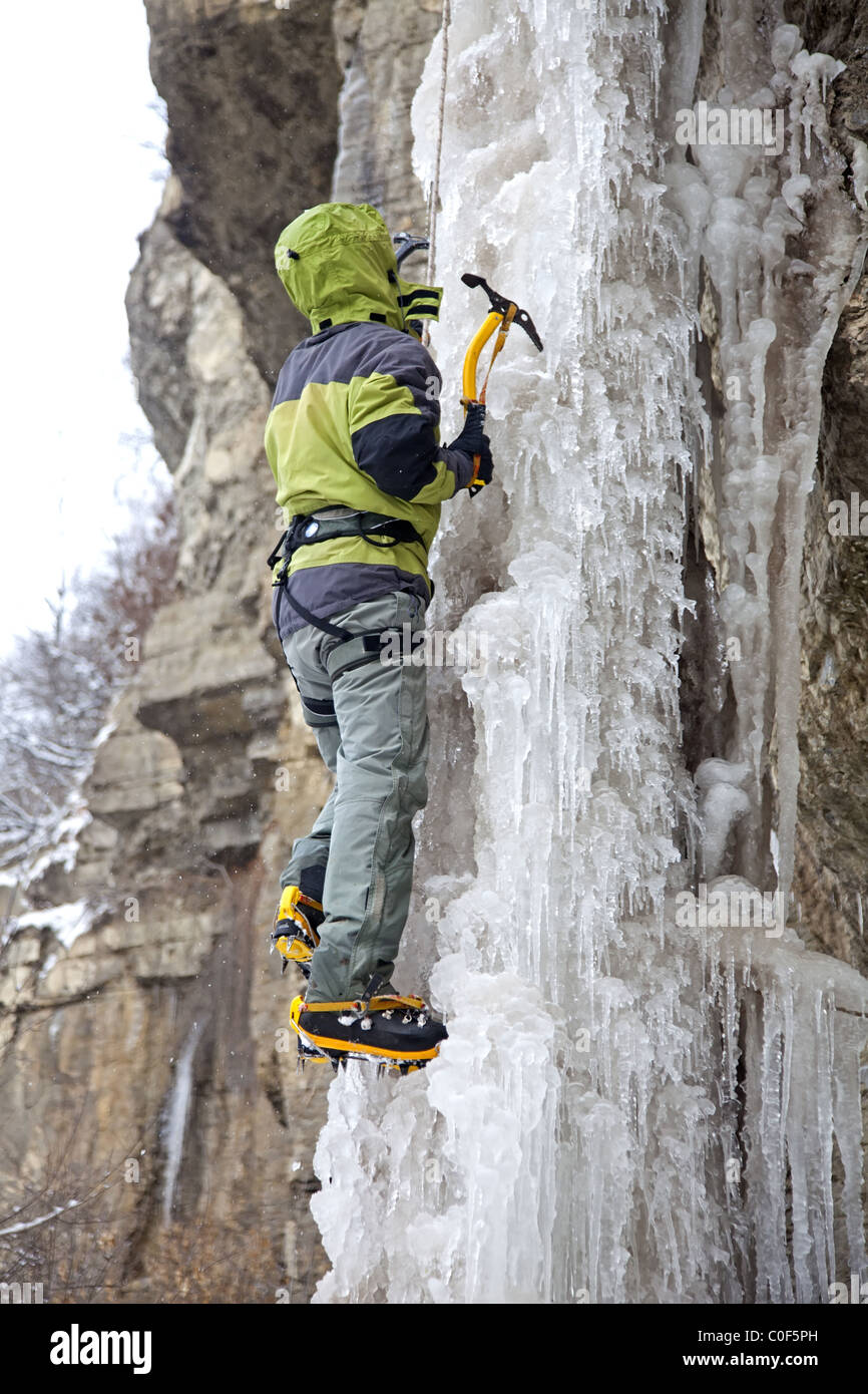 Man with ice axes and crampons climbing on icefall Stock Photo