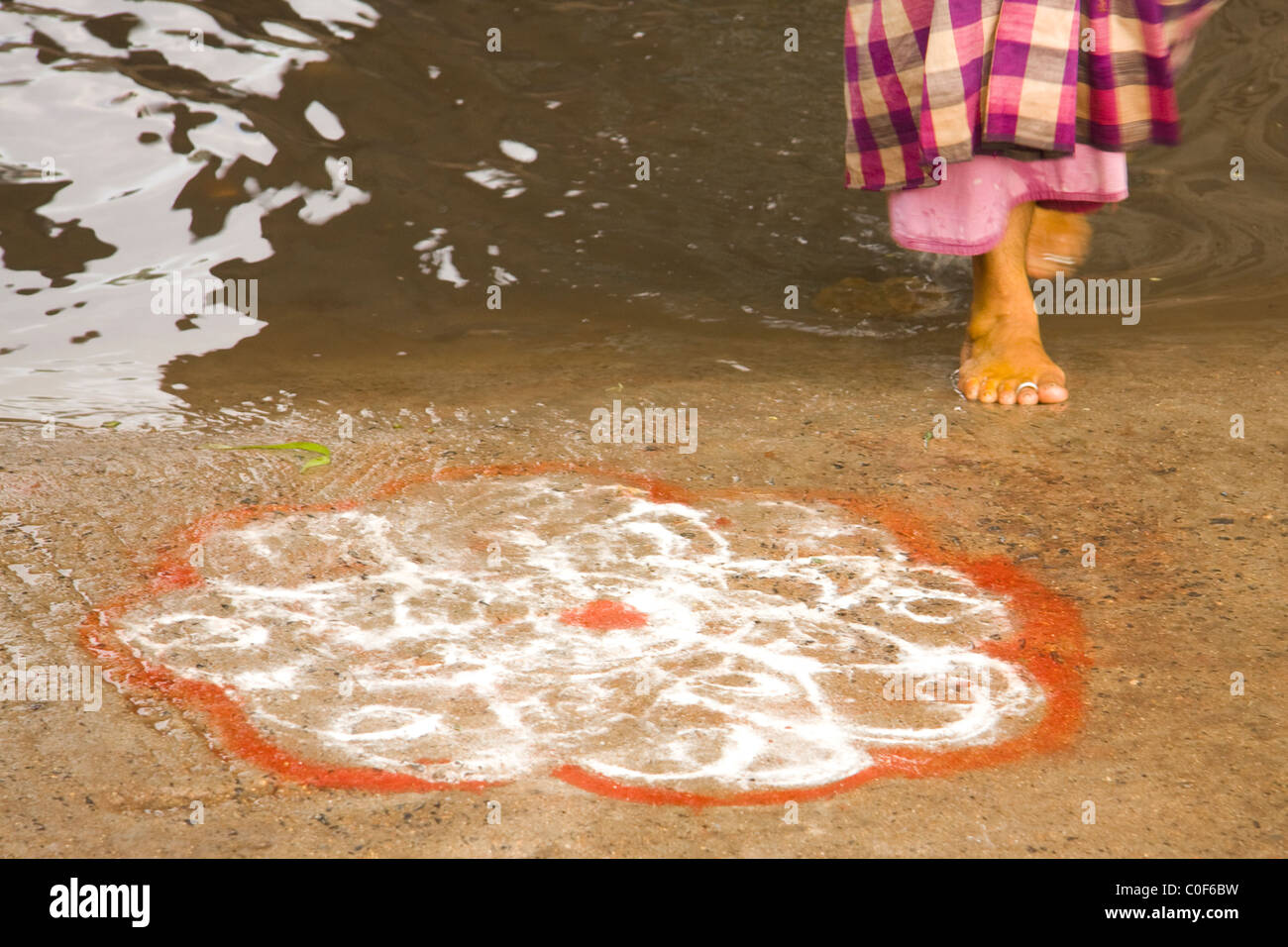 Barefoot Indian lady coming out from a Temple with a Kolam Stock Photo
