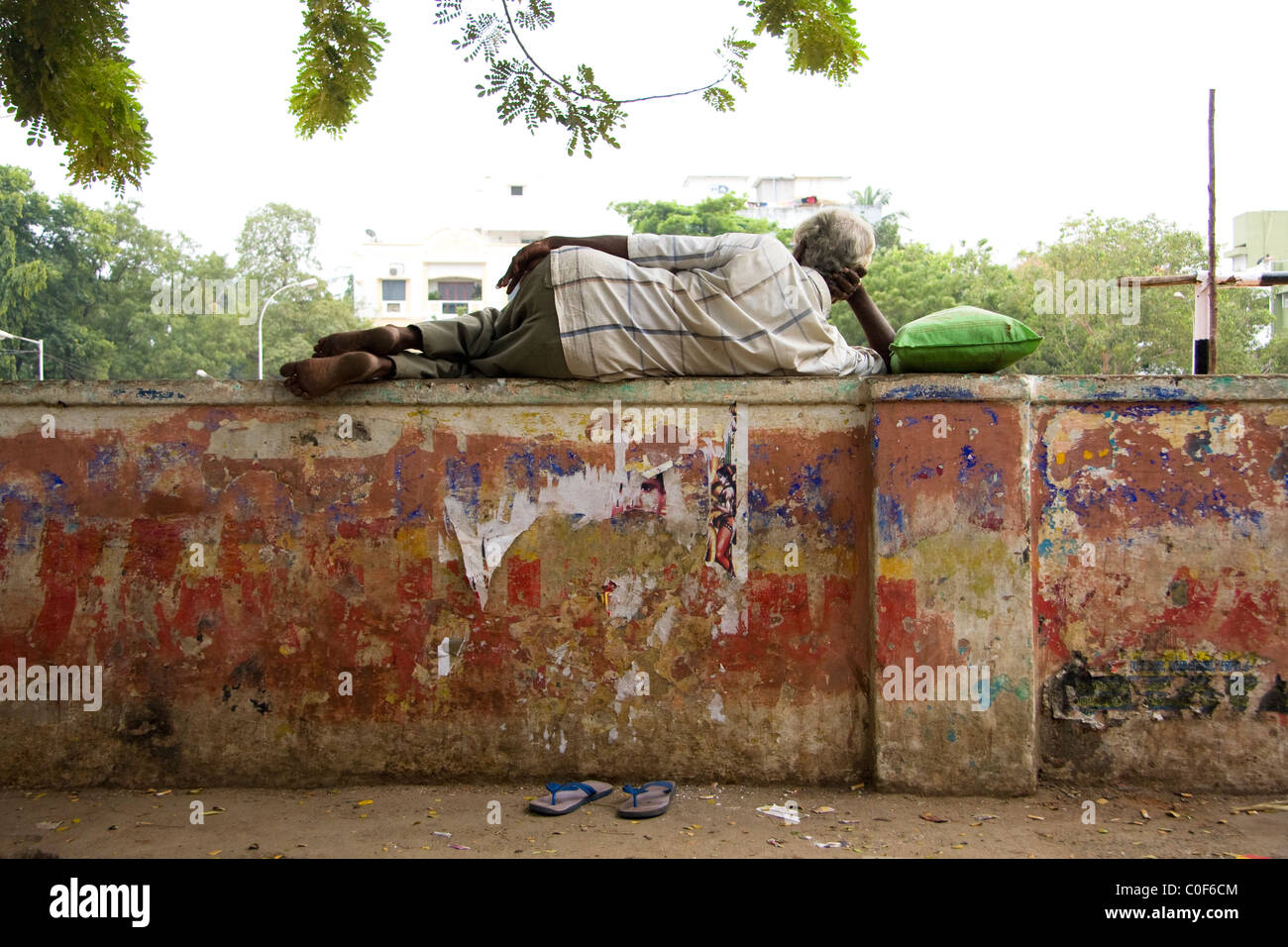 Indian man laying on a wall with a green pillow and blue flip flops. Stock Photo