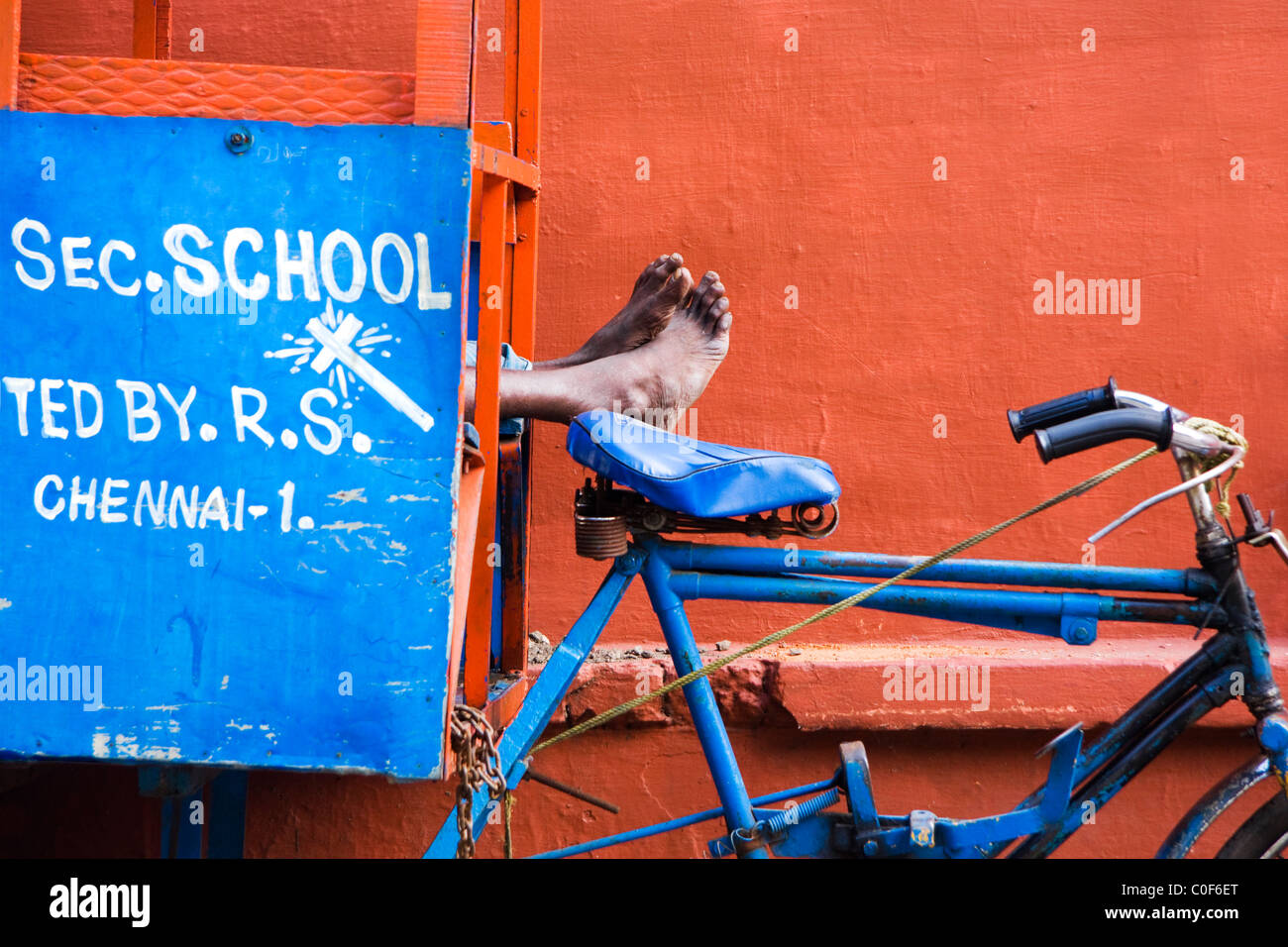 Rickshaw driver sleeping with its feet on the blue bicycle seat. Stock Photo