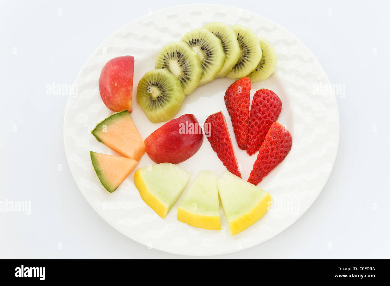 Five pieces of chopped fresh fruit salad on a white plate to illustrate five a day. Stock Photo