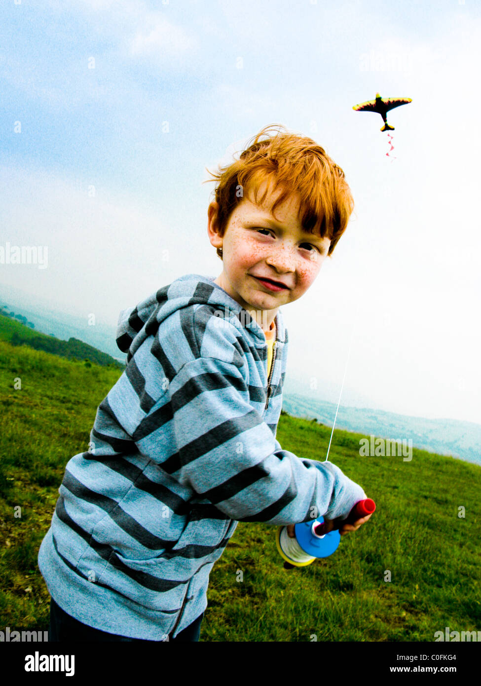Small boy on a hill top in South Wales UK running in the wind and flying a kite Stock Photo