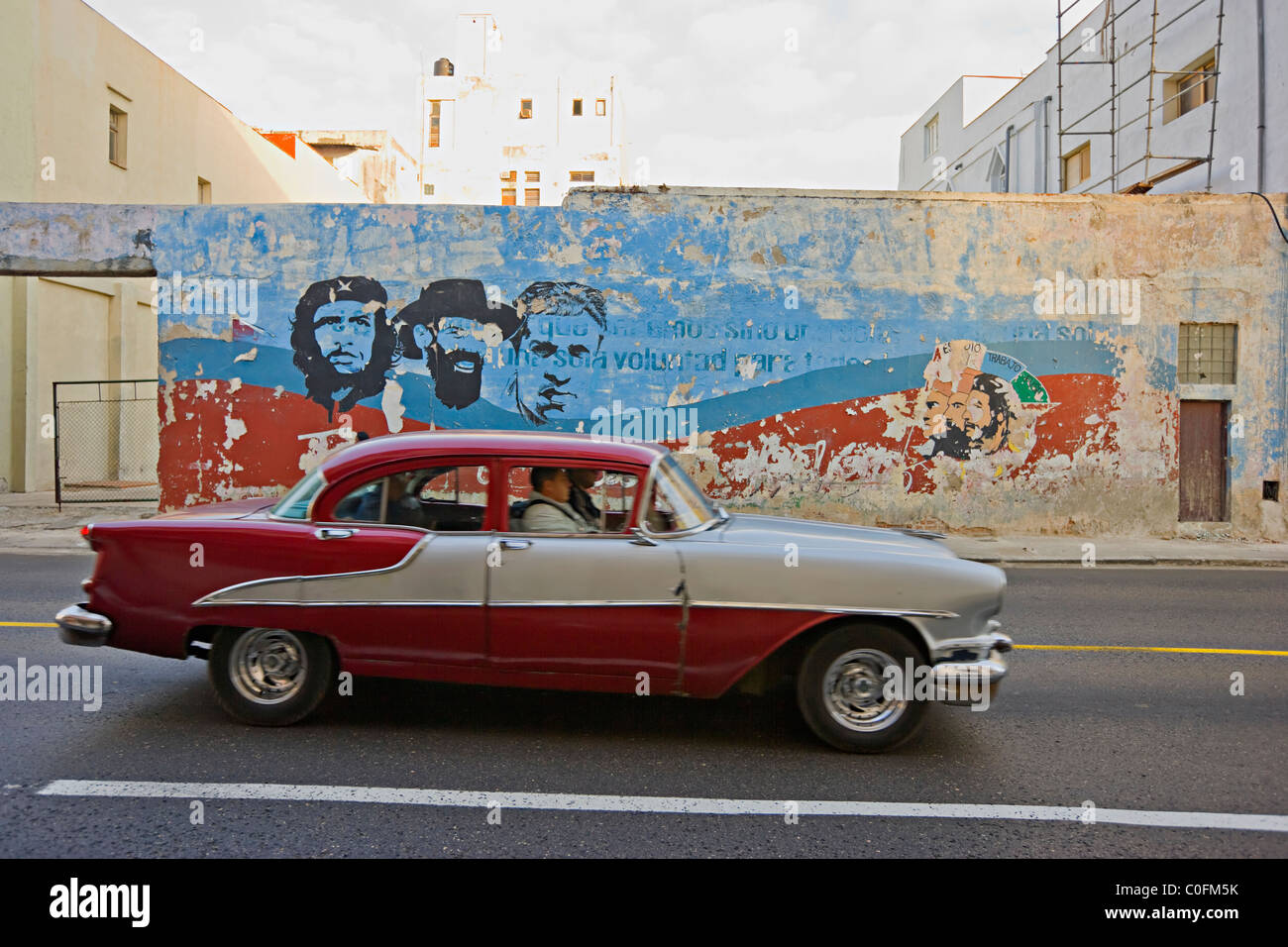 An old American 1950s automobile driving past a painted mural of Che Guevara in Havana Cuba Stock Photo