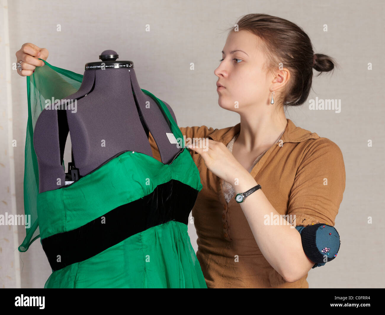 A young seamstress adjusts the green evening dress on the dummy. Stock Photo