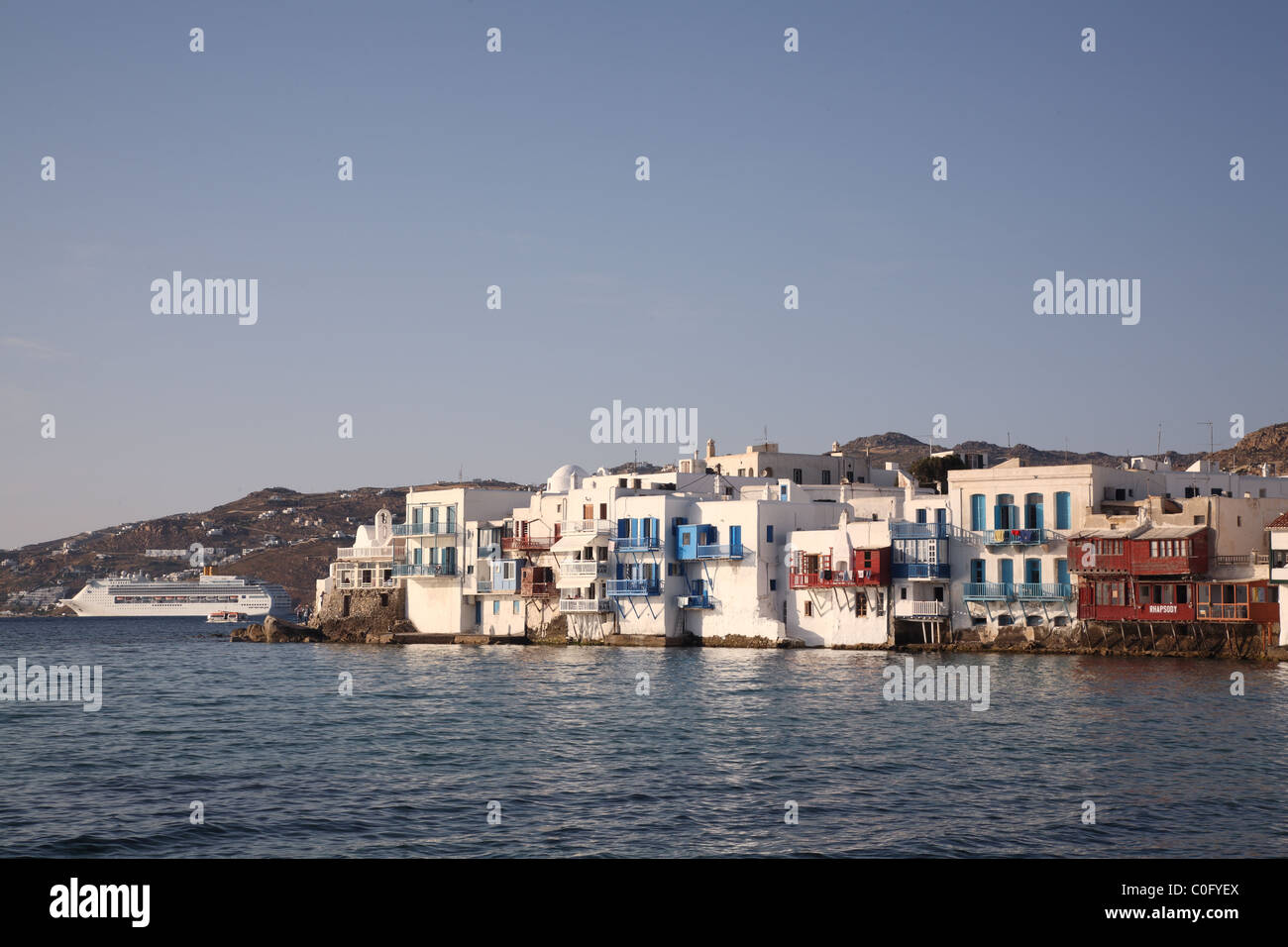 Little Venice with cruise ship behind basking in late afternoon sun, Mykonos Town (Chora), Mykonos, Cyclades, Greece Stock Photo