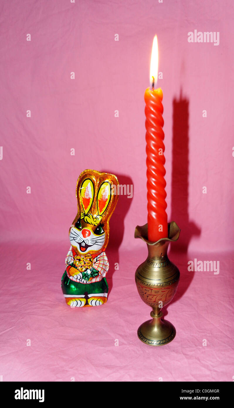 Chocolate hare in a colorful wrapper and a burning candle in a candlestick Stock Photo