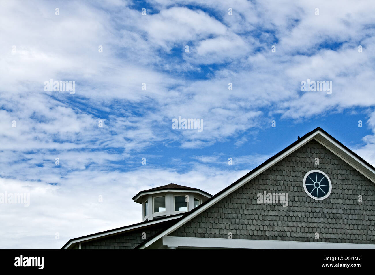 Gable of a grey house showing against a blue sky with puffy clouds Stock Photo