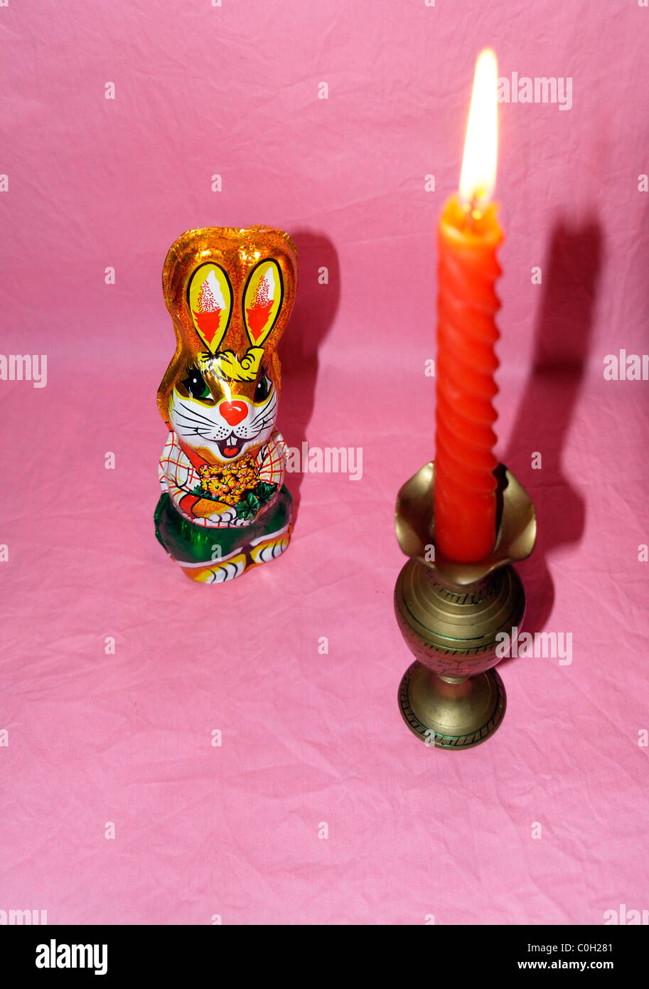 Chocolate hare in a colorful wrapper and a burning candle in a candlestick Stock Photo