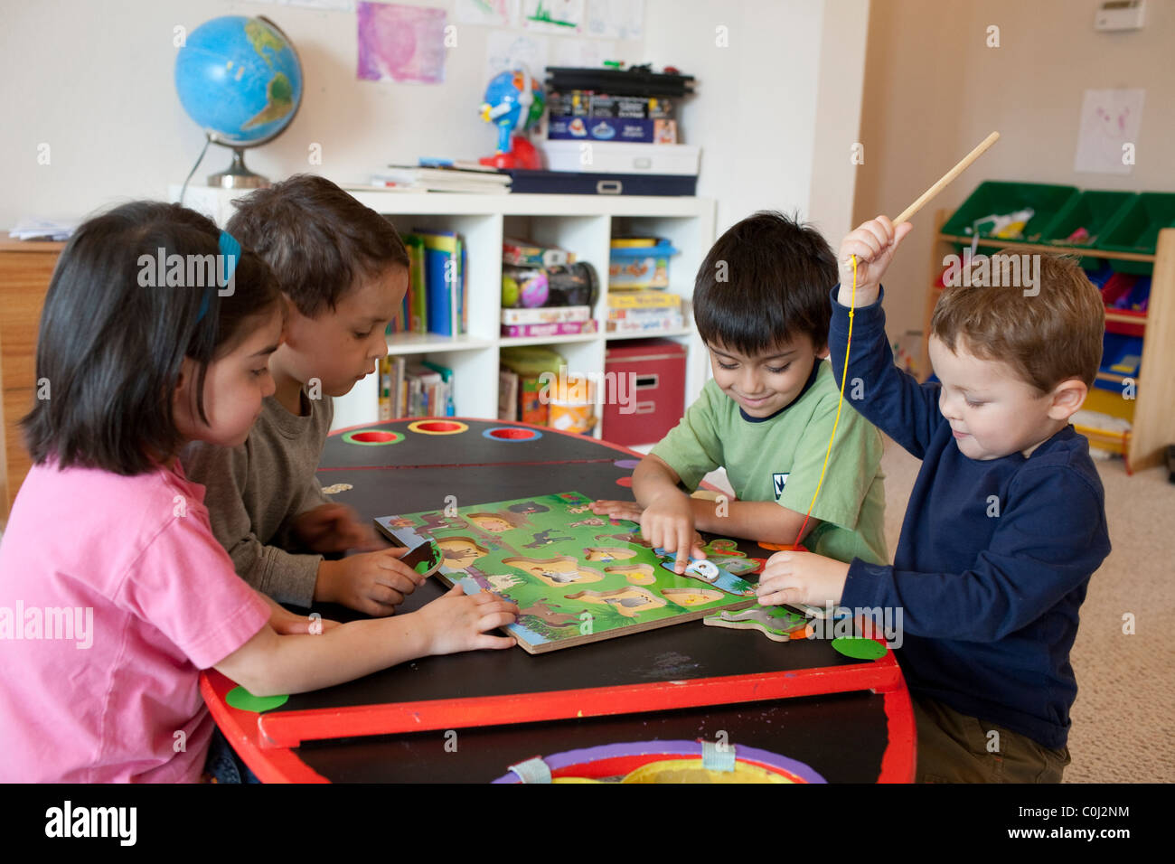 Mexican-American children, ages six, five, four and three, cooperate to put together a wooden puzzle at home in Austin Texas Stock Photo